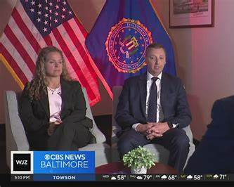 CBS News Baltimore interview footage with two people seated in front of an FBI seal.